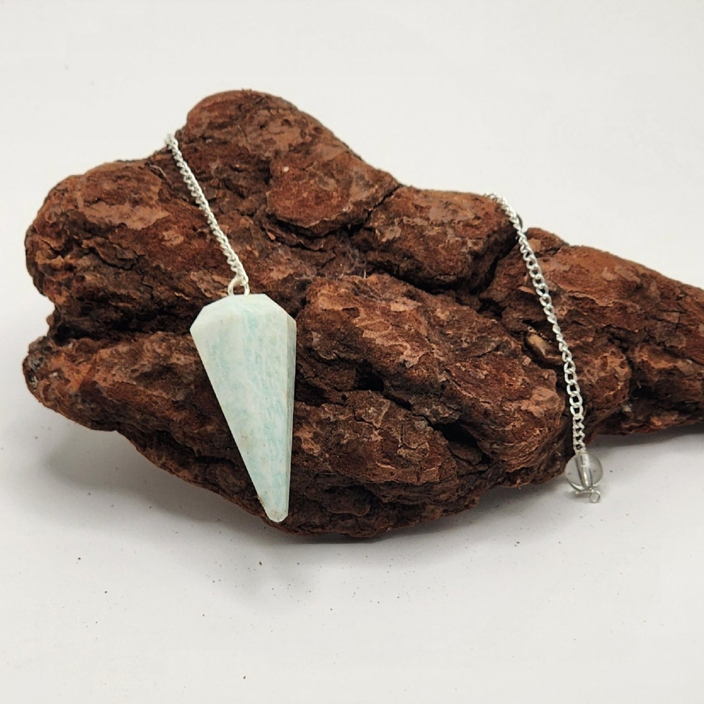 single amazonite pendulum draped over a textured piece of wood