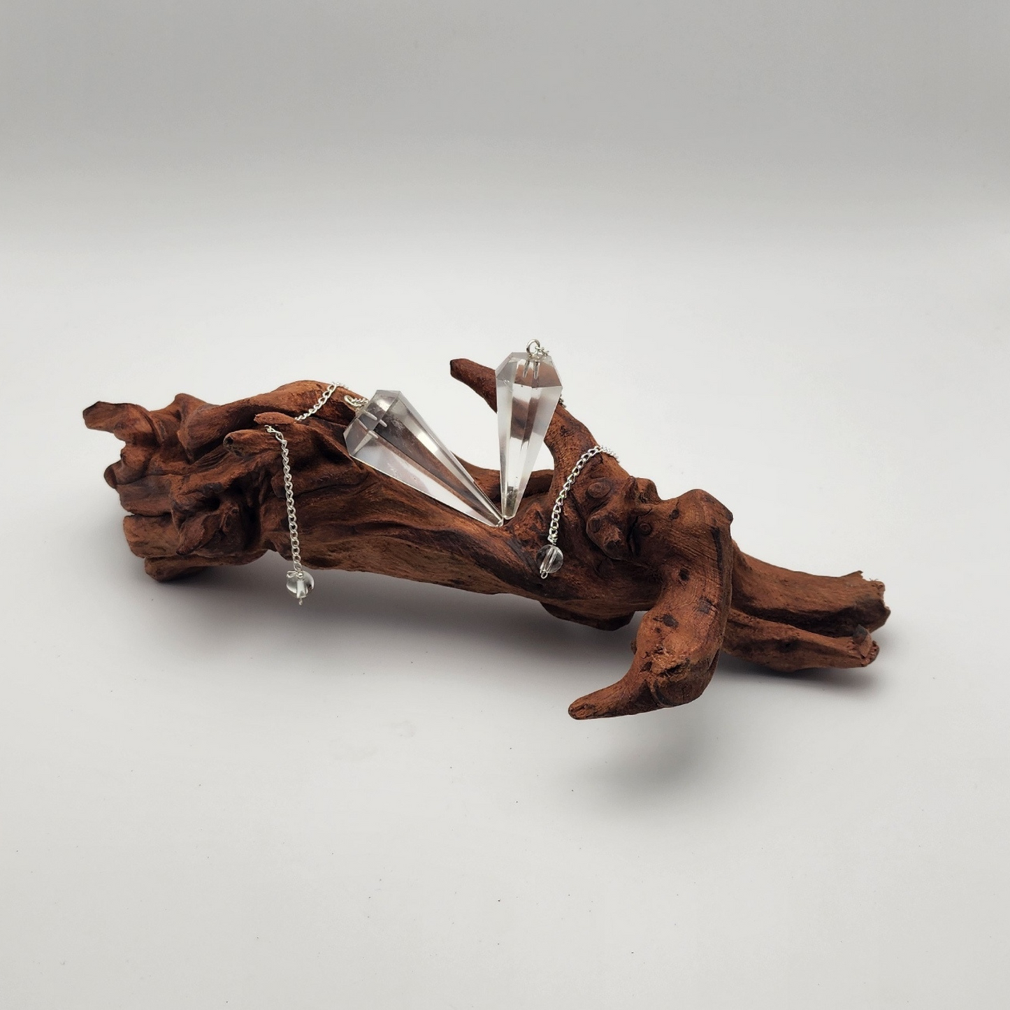 two clear quartz pendulums draped over a dark piece of wood with the chains draped around the wood