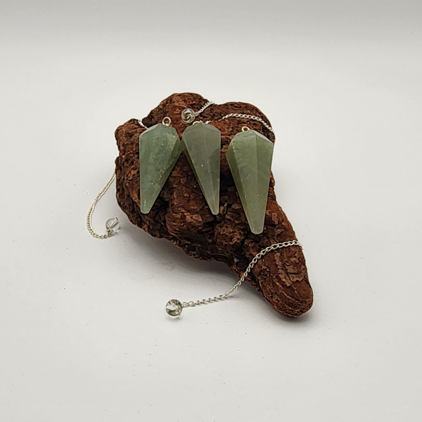 Three green aventurine pendulums placed on an aged piece of wood with two of the pendulum chains visibe.