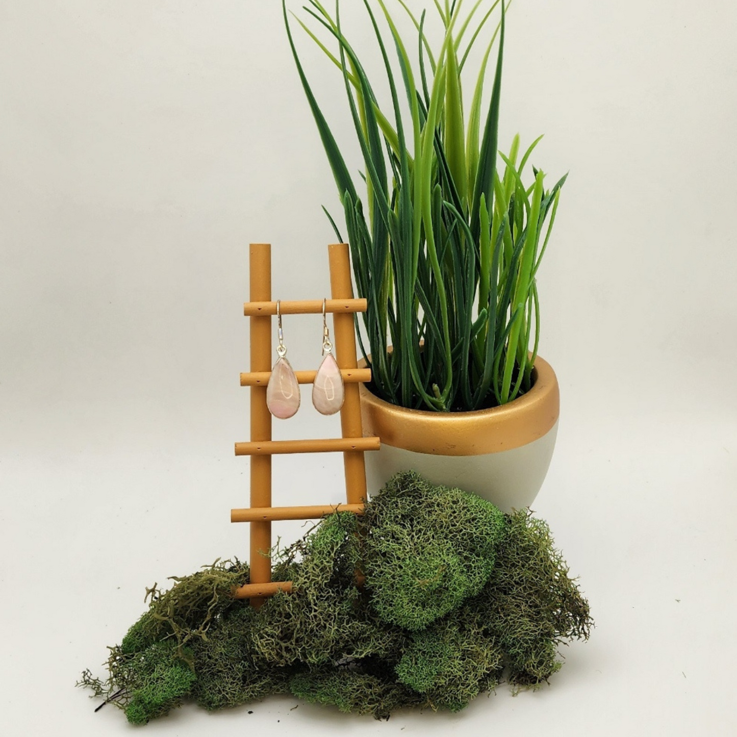 single pair of ice cream opal earrings displayed on a mini wooden ladder. there is a potted plant behind and to the right and a tuft of moss below the ladder.