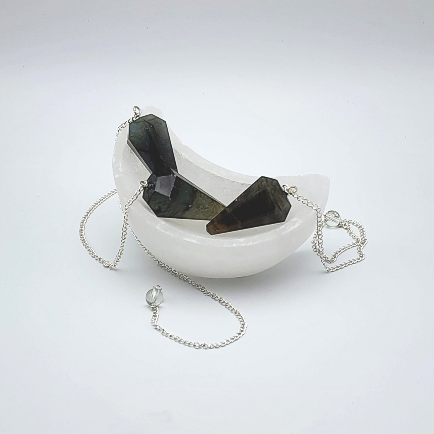 three labradorite pendulums inside of a moon shaped selenite bowl