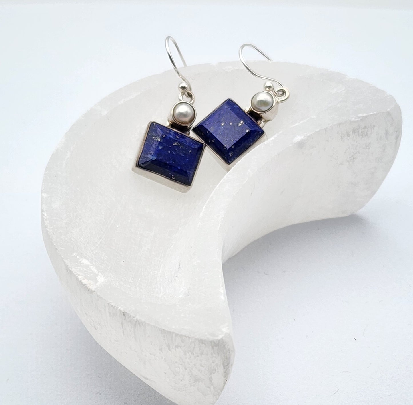 a pair of lapis and pearl earrings placed in a selenite moon shaped bowl