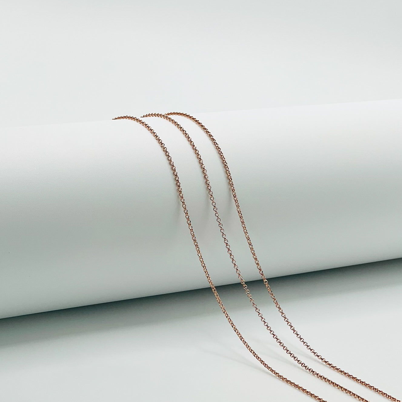 three rose gold rolo chains draped over a white cylinder with a white background