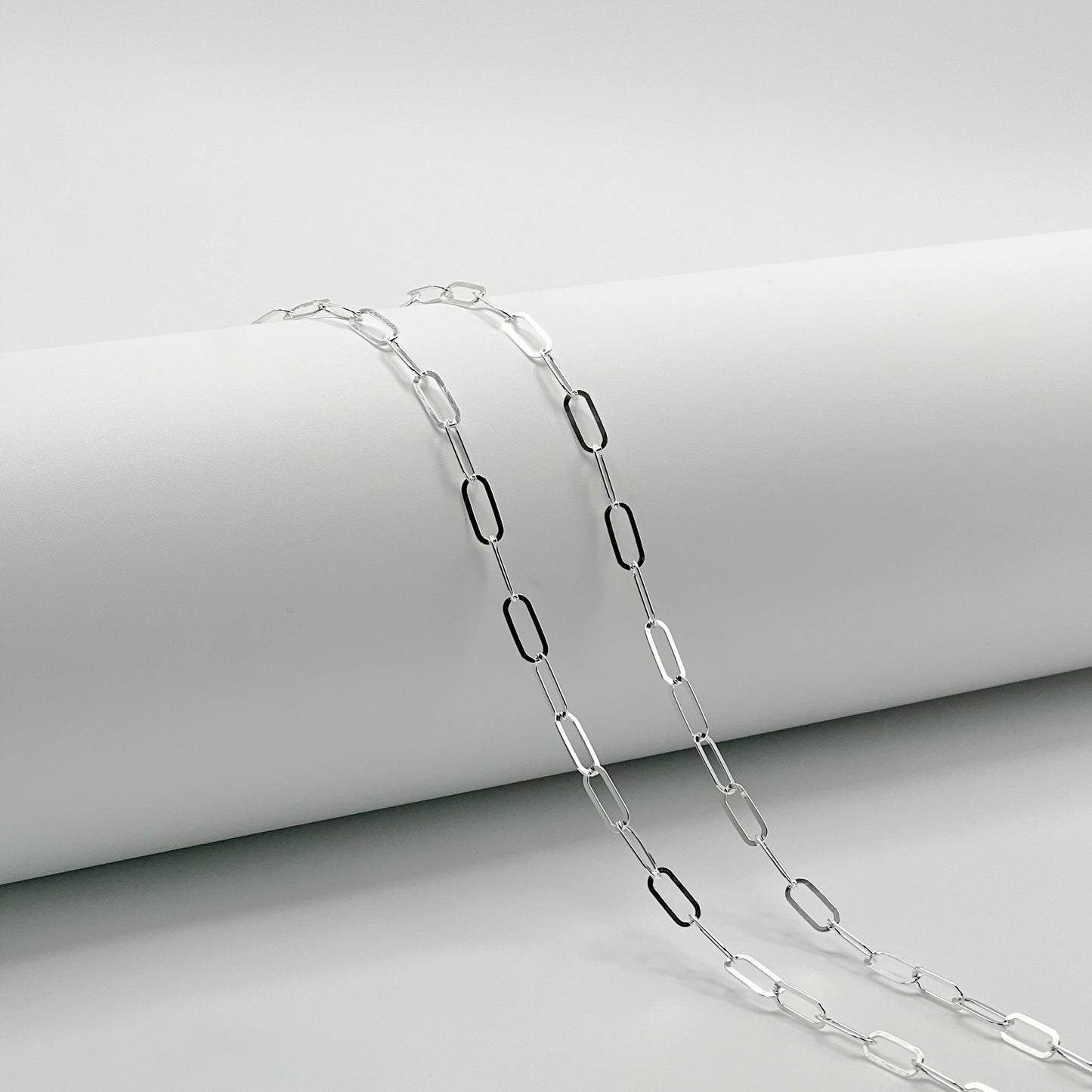 two paperclip chains are draped over a white cylinder with a white background.