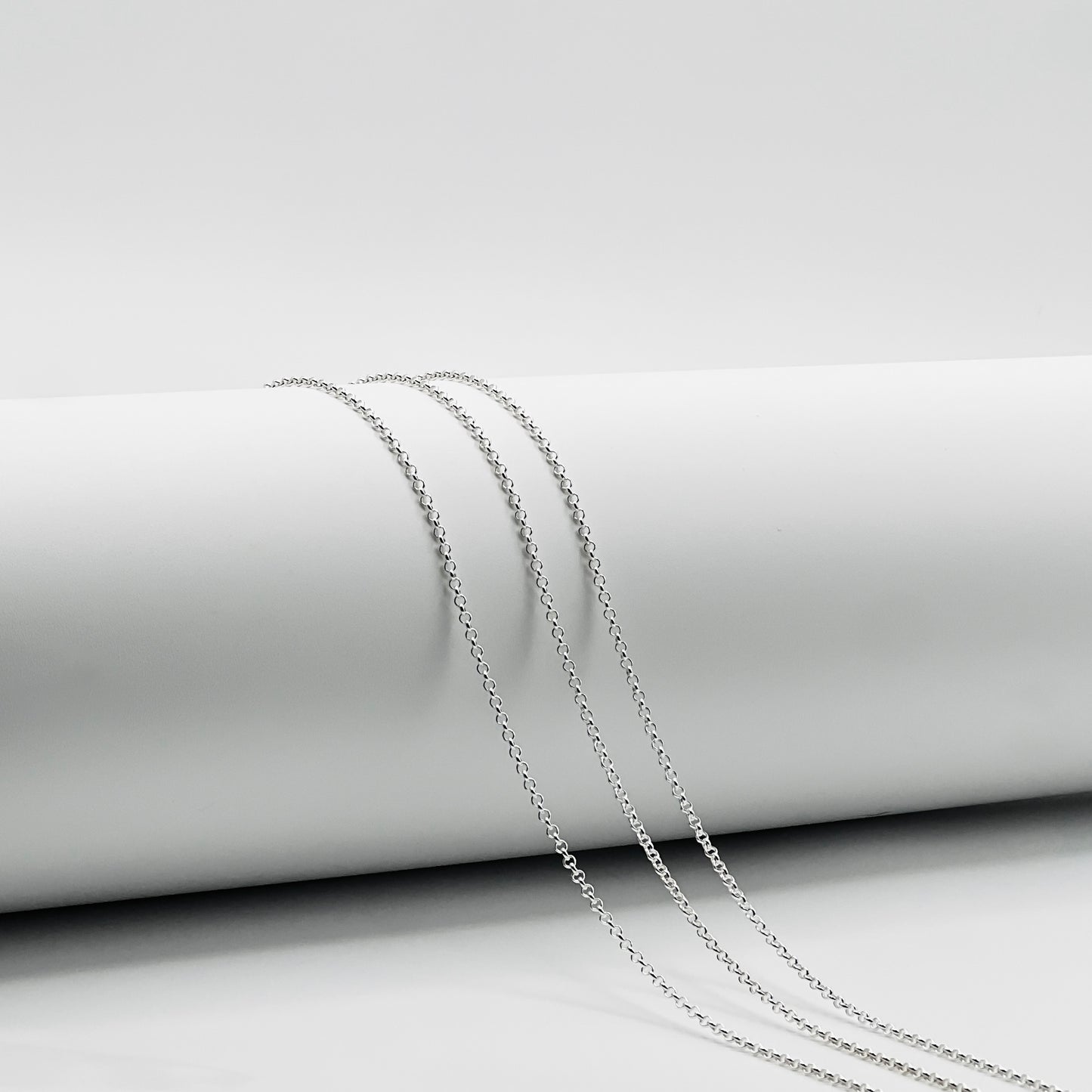 three rolo chains draped over white cylinder with white background