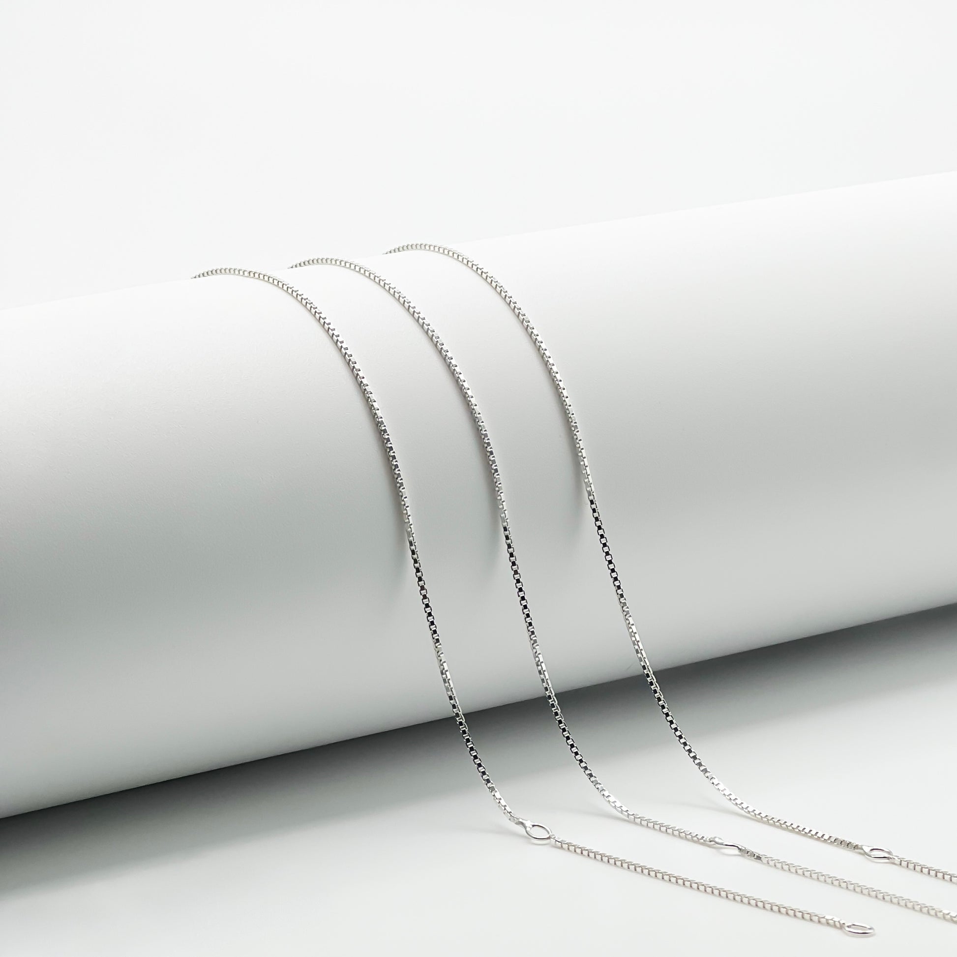 three adjustable box chains draped over a white cylinder with a white background. Two closure points that make this style adjustable are visible.