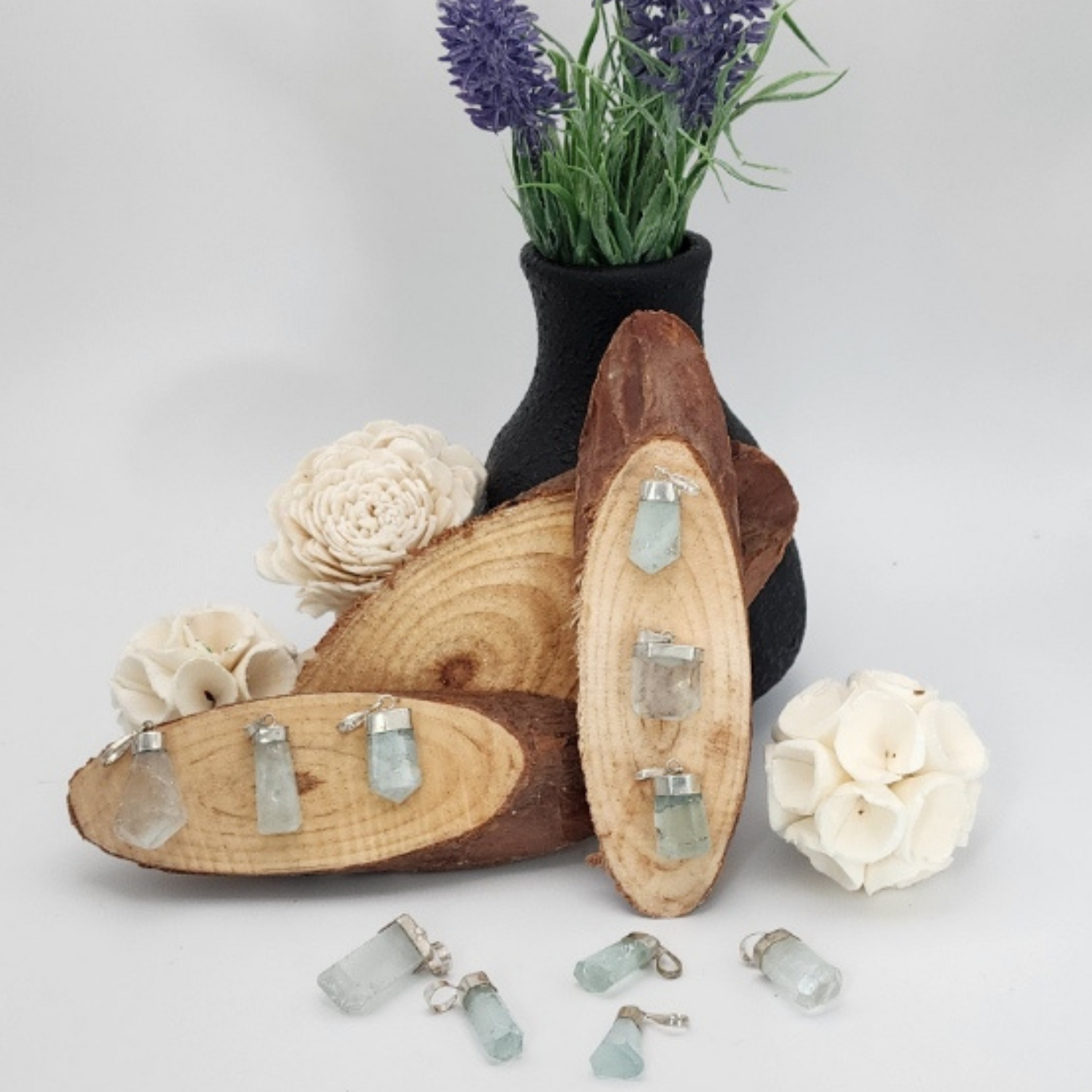 Wood slices displaying aquamarine gemstone pendants and flowers on a plain background.