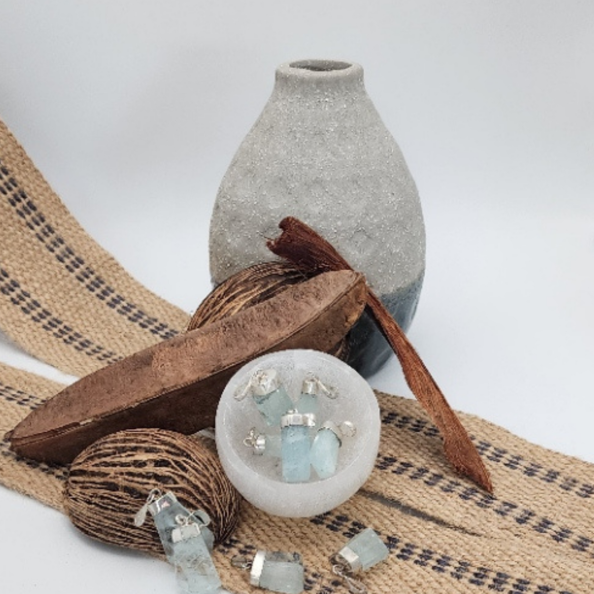 Aquamarine pendants in a selenite trinket bowl with natural elements like stones and fibers.