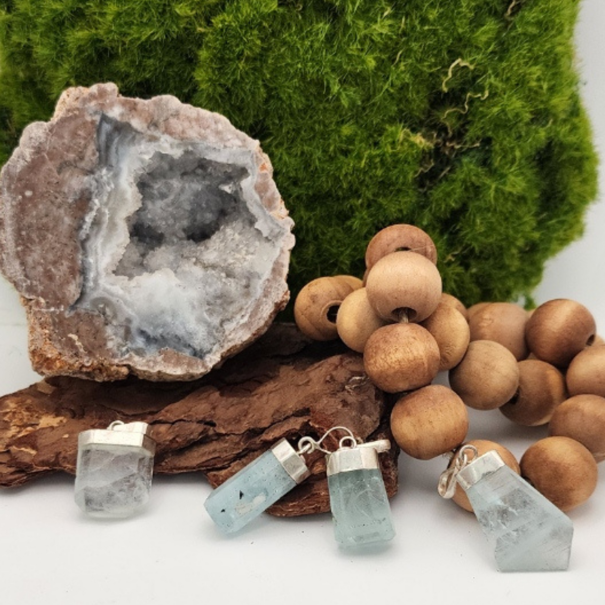 Geode, wooden beads, and aquamarine pendants on a white surface with green moss background