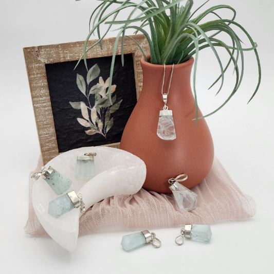 Terracotta vase with a plant, aquamarine pendants on a white surface.