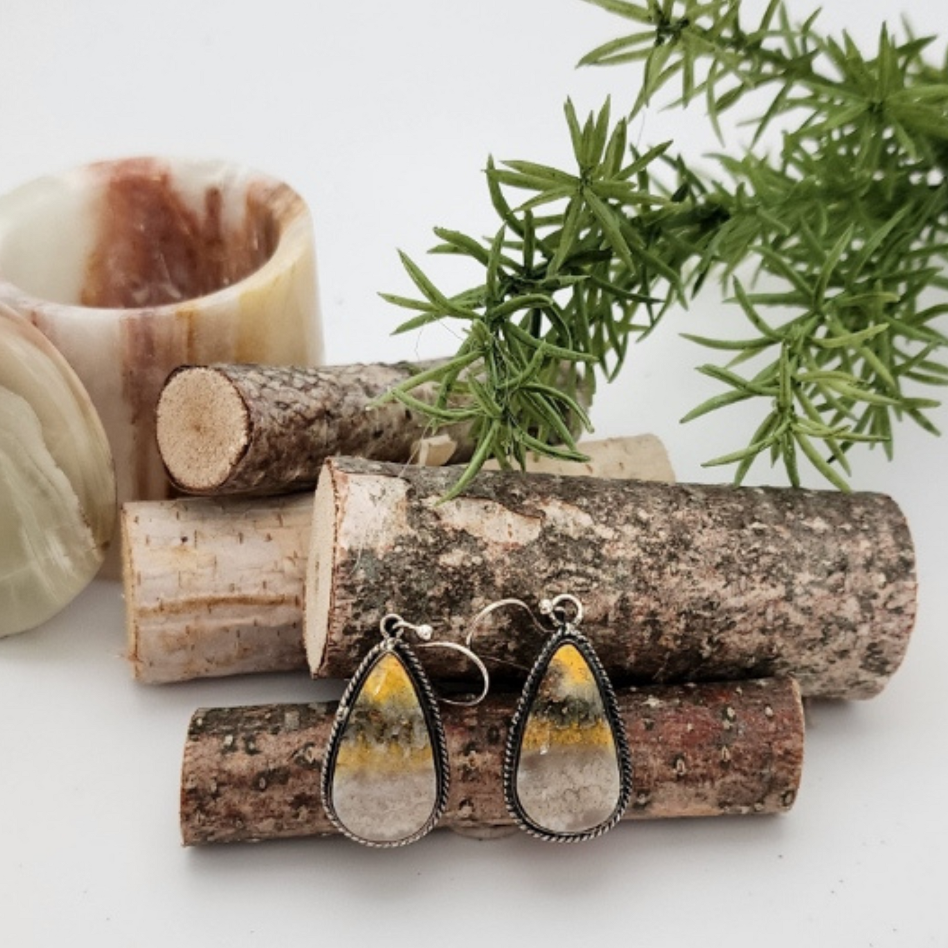 Teardrop-shaped bumblebee jasper earrings on mini wood logs surrounded by other natural elements