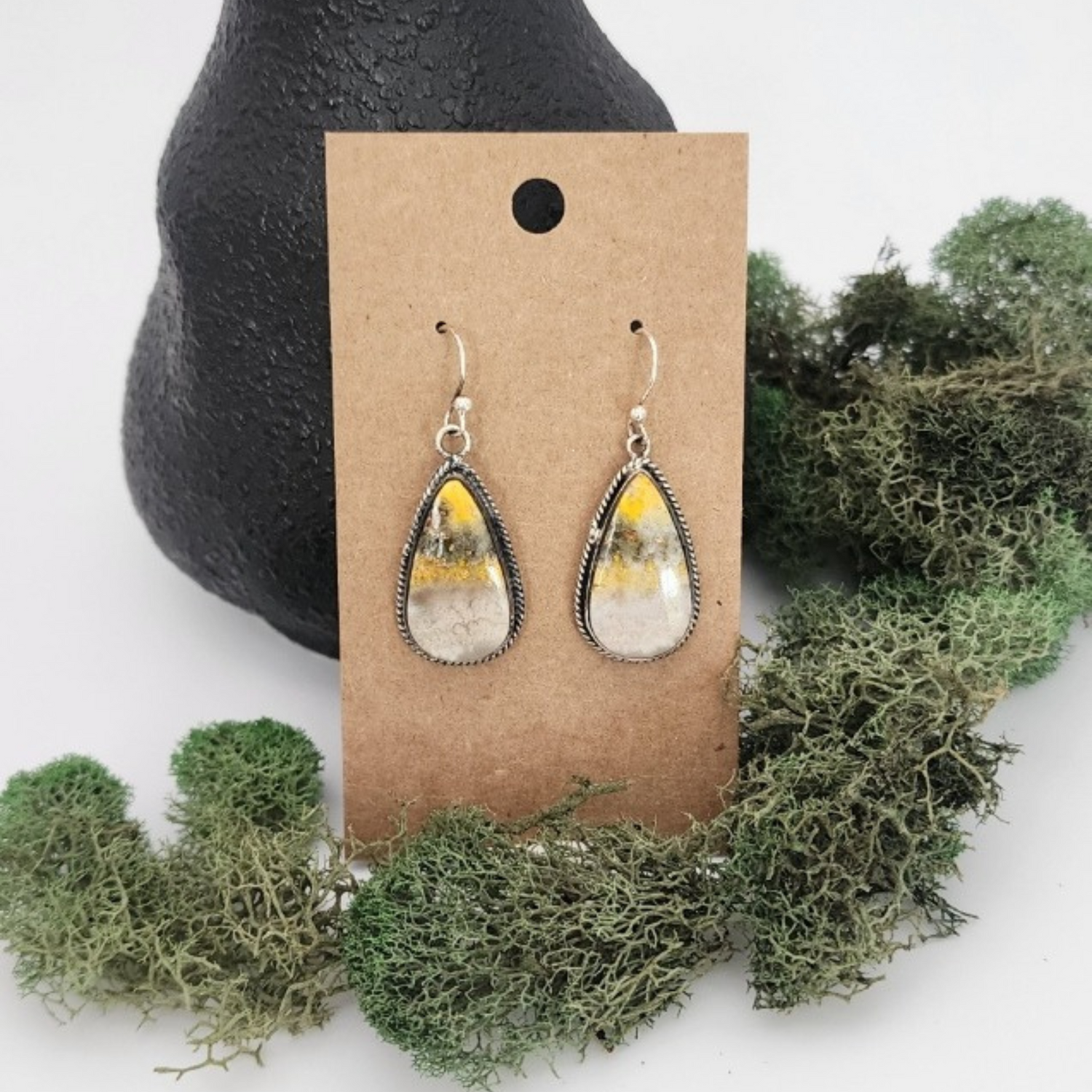 Teardrop-shaped Bumblebee jasper earrings on a brown card with greenery in the background.