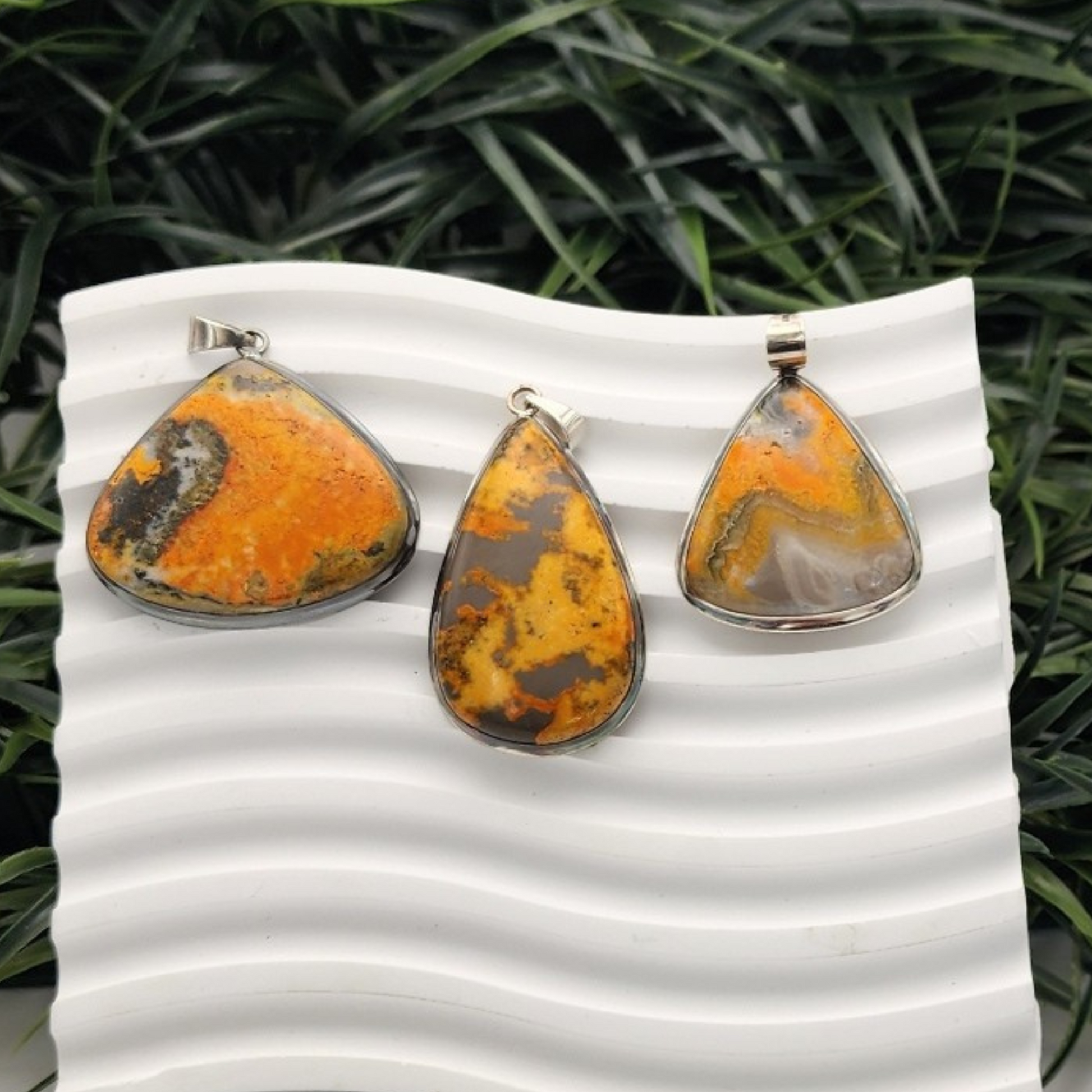 three different bumblebee jasper pendants displayed on a white squiggle background with grass in backdrop