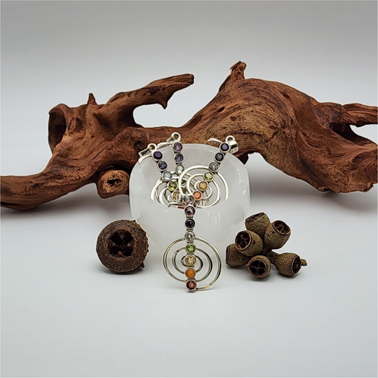 Four chakra pendants in a small selenite bowl with a piece of wood and dried acorns surrounding the bowl.
