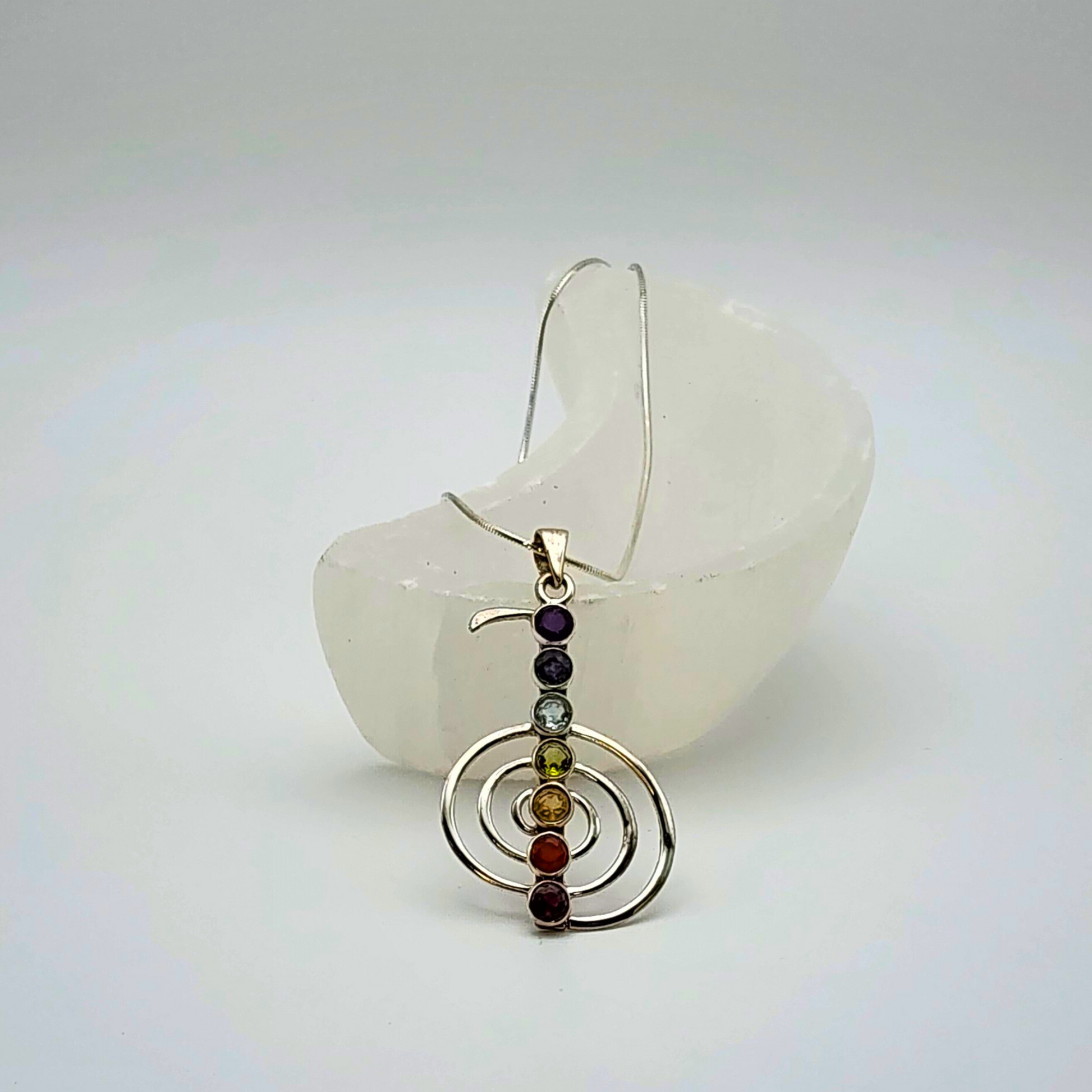 A single chakra pendant on a snake chain laying in a small moon shaped selenite bowl.