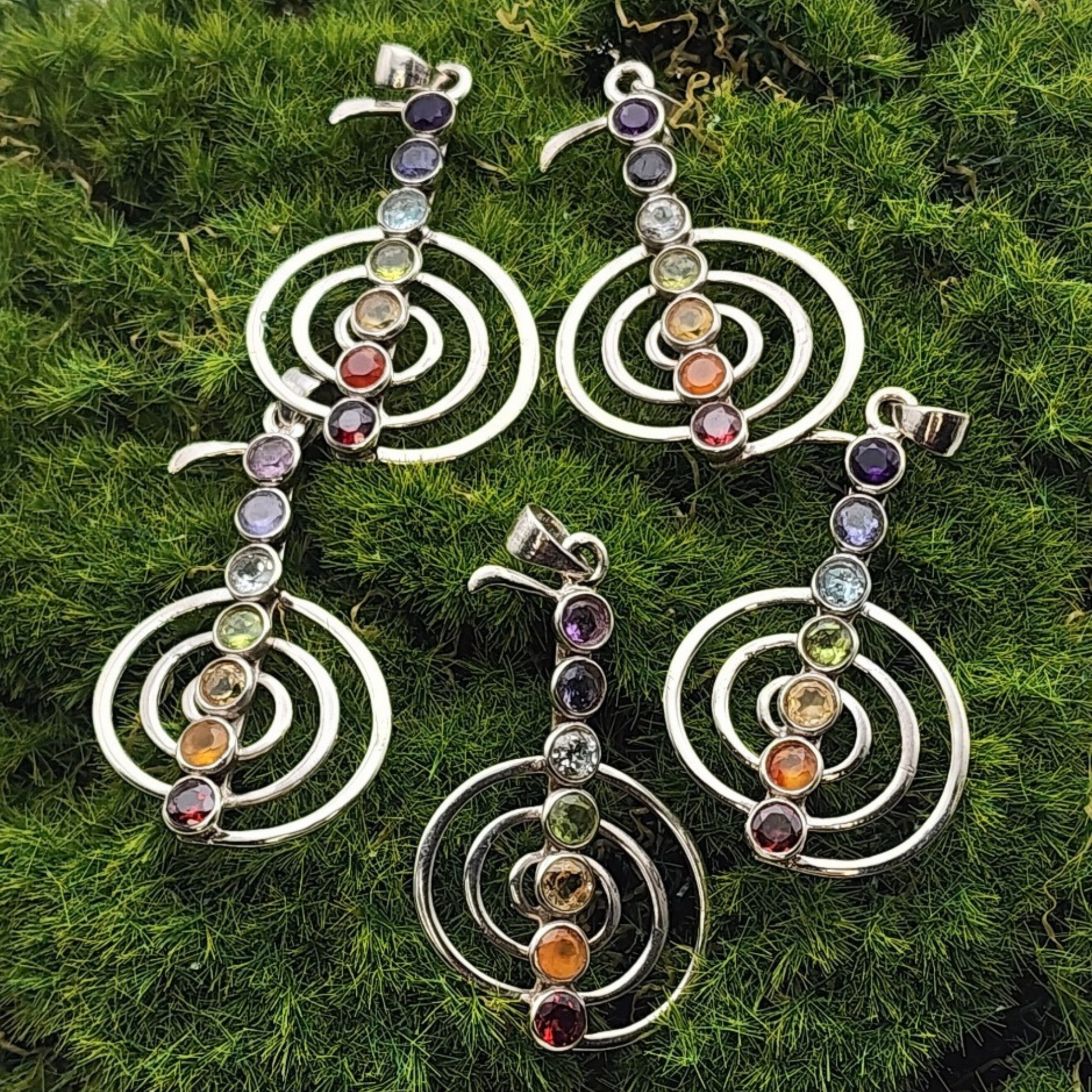 Five chakra pendants laid on a patch of green moss.