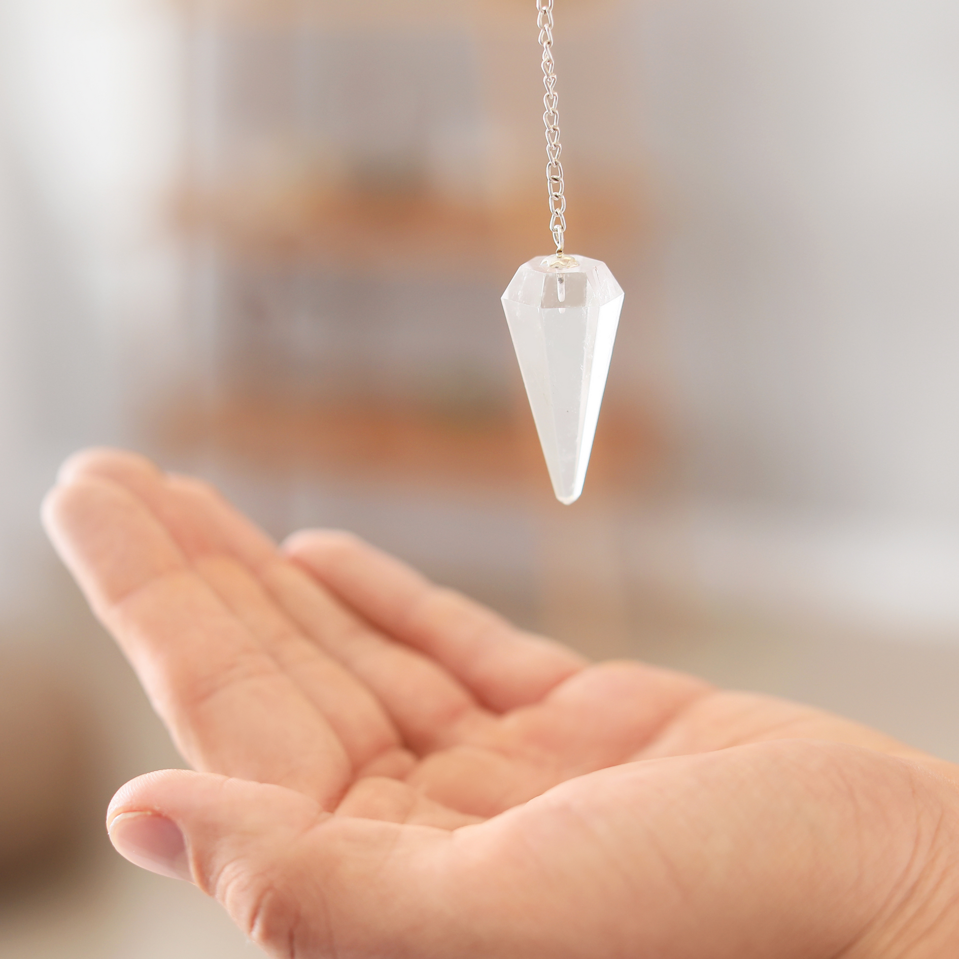 a clear quartz pendulum suspended over an open palm