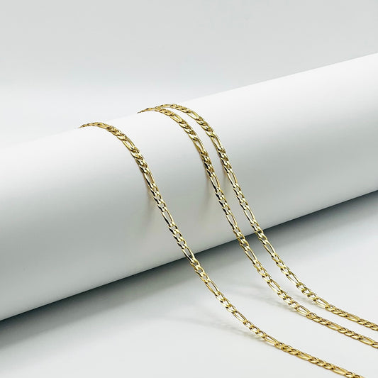 three gold figaro chains are draped over a white cylinder with a white background.