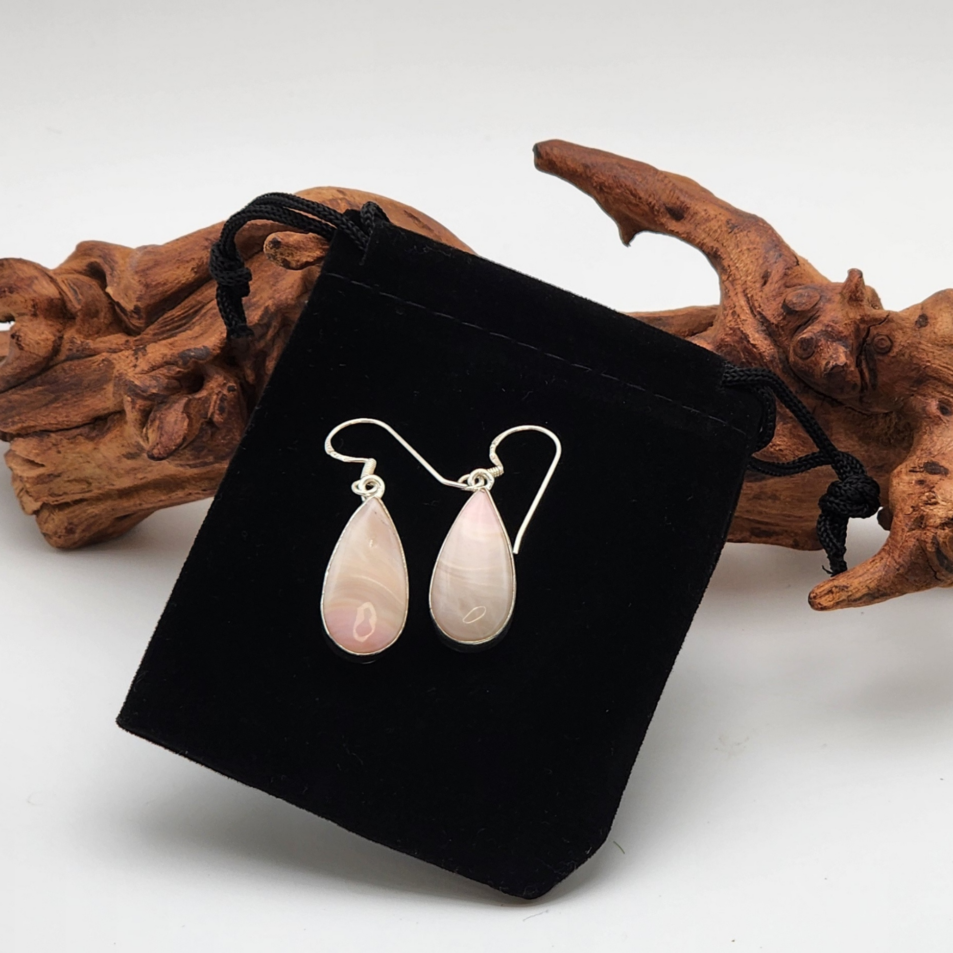 single pair of ice cream opal earrings placed on a black velvet jewelry bag with a piece of aged wood behind the earrings.