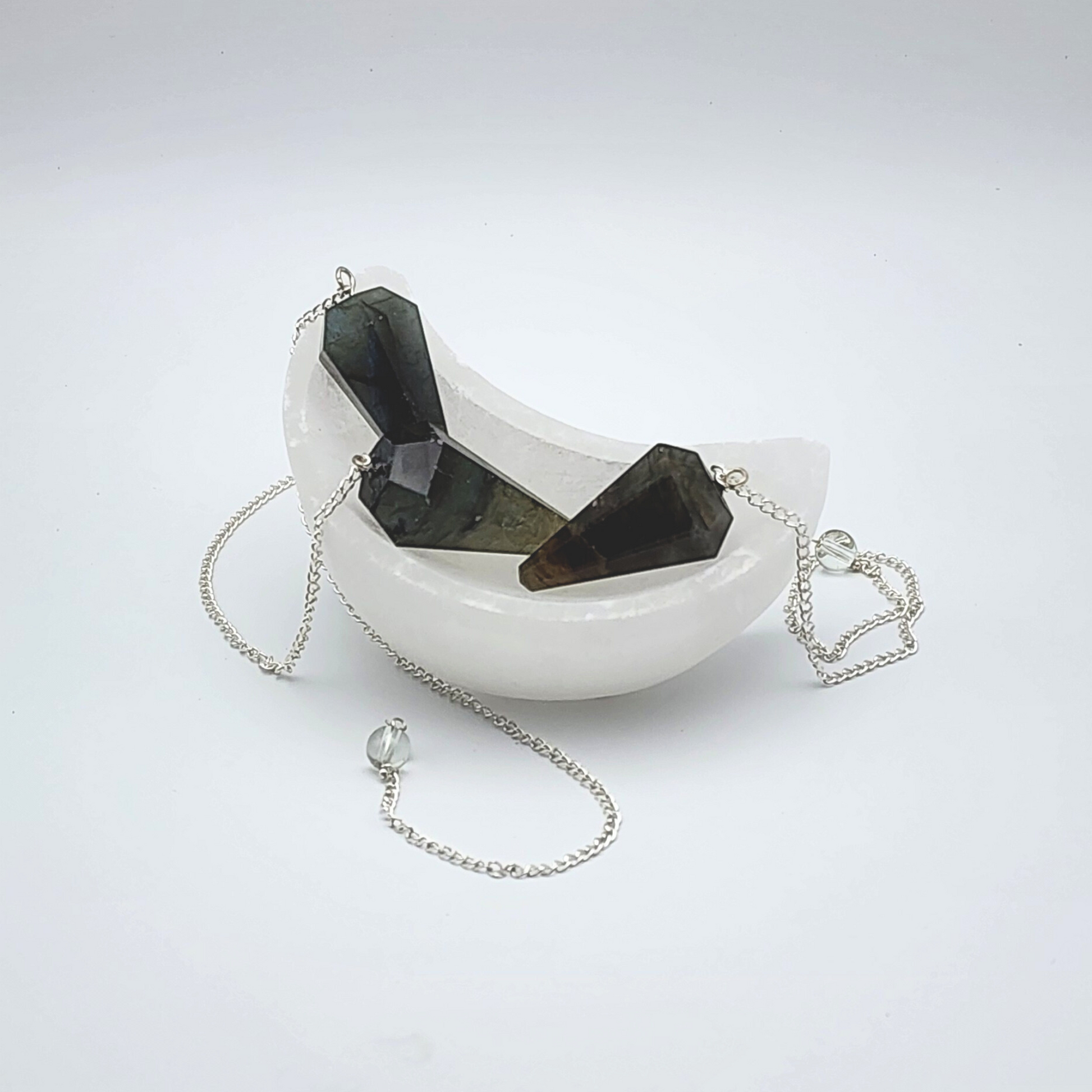 three labradorite pendulums inside of a moon shaped selenite bowl