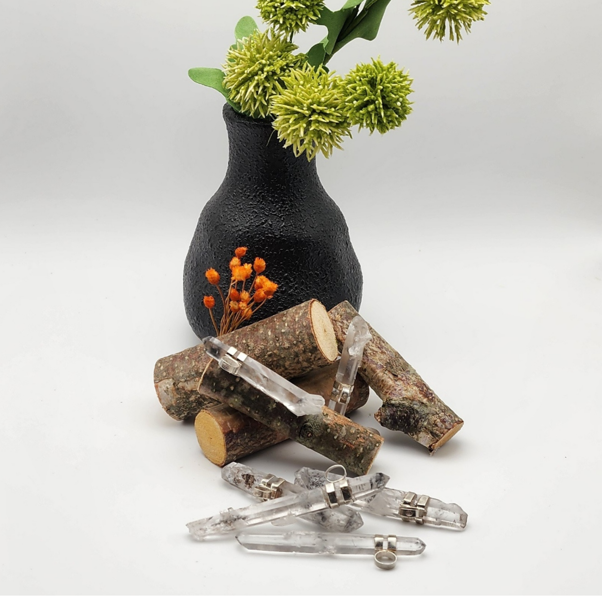 two lemurian quartz pendants are displayed on a stack of small birch sticks with four lemurian quartz pendants in front of the sticks staged and arranged in a moody Bloom and Glow aesthetic scene.