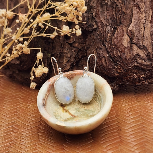 Pair of faceted moonstone earrings placed in a small onyx bowl with a decorative background.