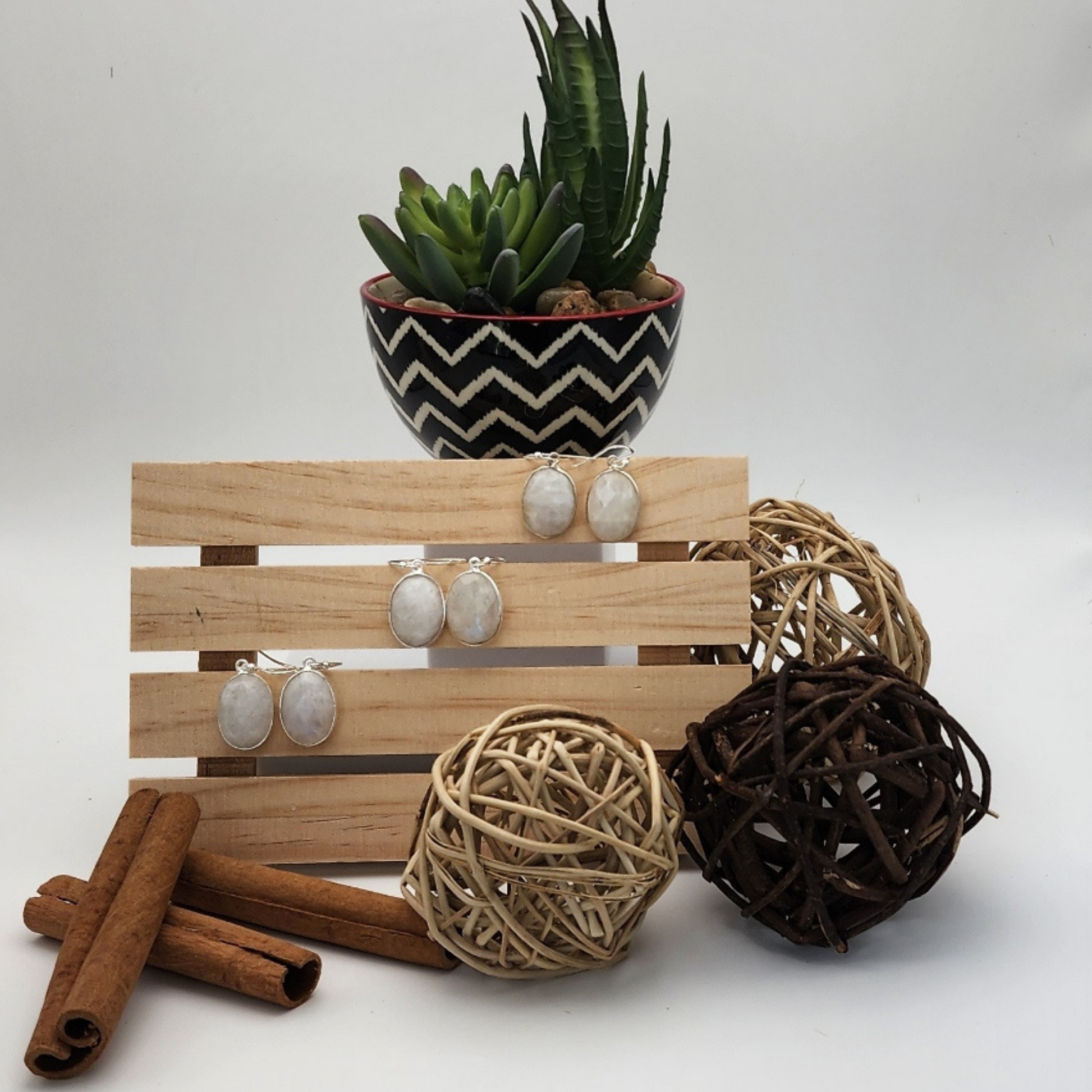 three pairs of faceted moonstone earrings displayed on a natural wood trivet staged and arranged in a moody Bloom and Glow aesthetic scene.