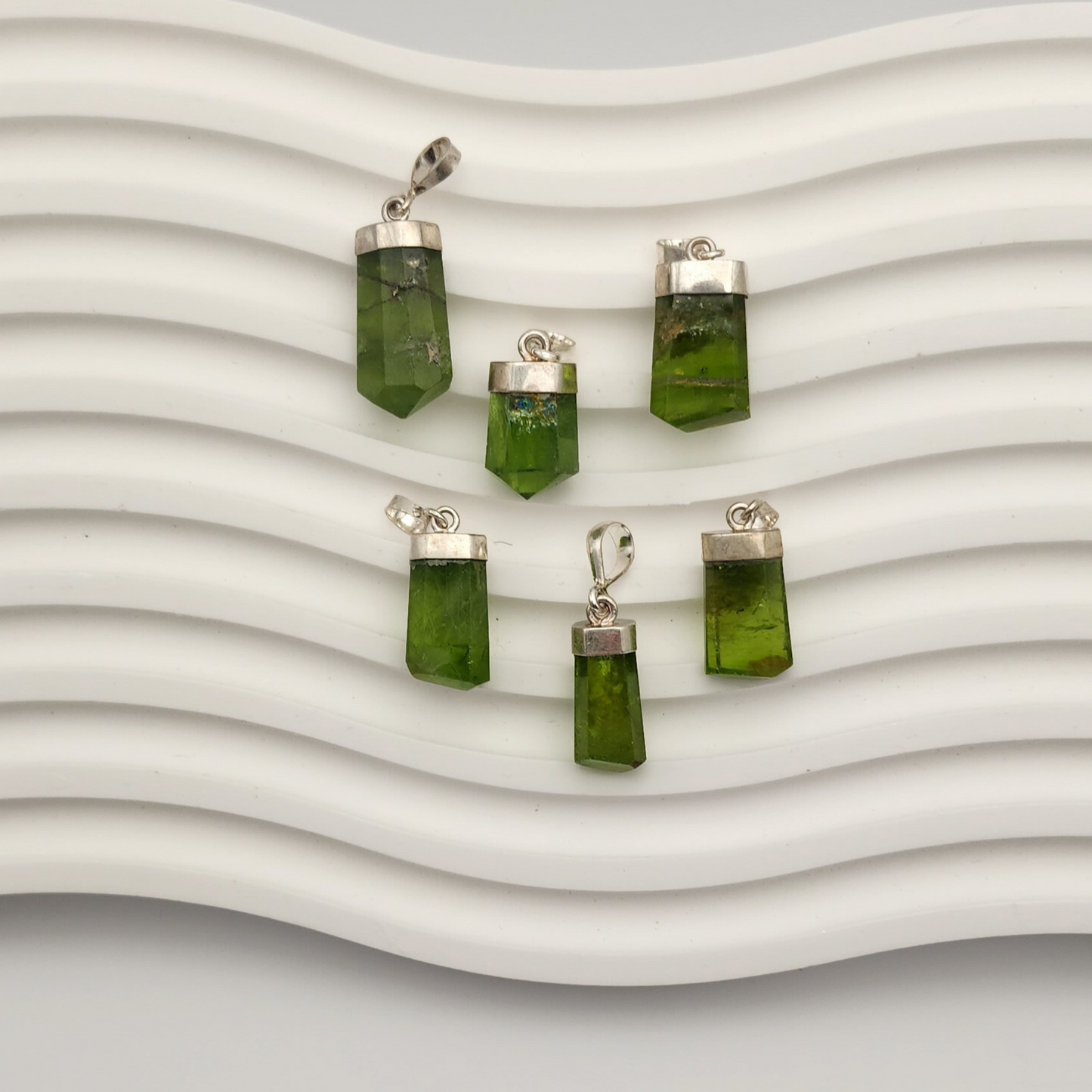 Six peridot pendants placed on a while squiggly background