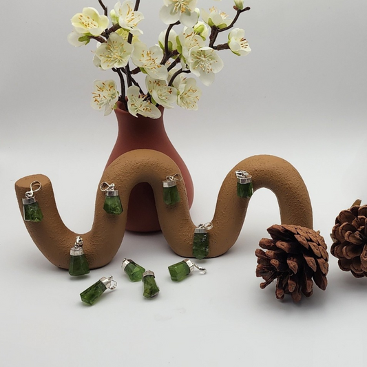 ten peridot pendants displayed on and around a brown swingle statue staged and arranged in a moody Bloom and Glow aesthetic scene.