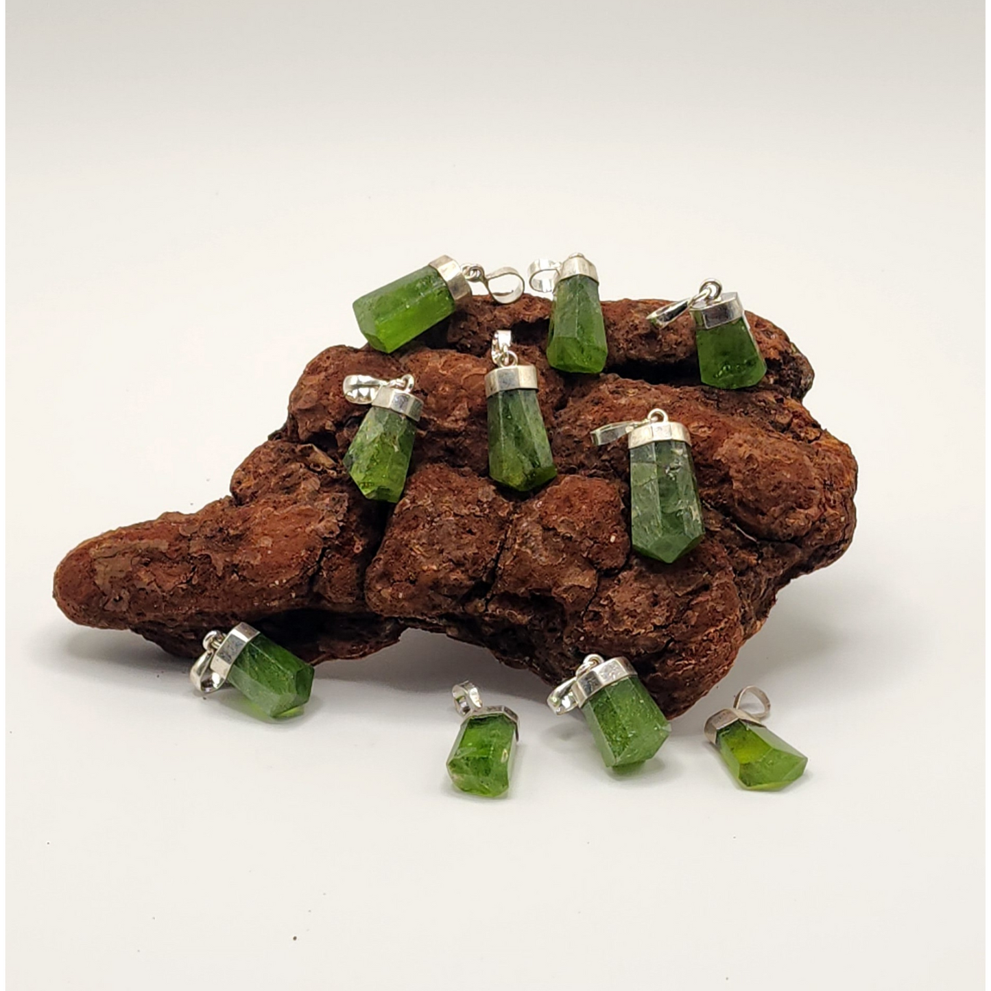 ten different peridot pendants placed on and around a piece of wood