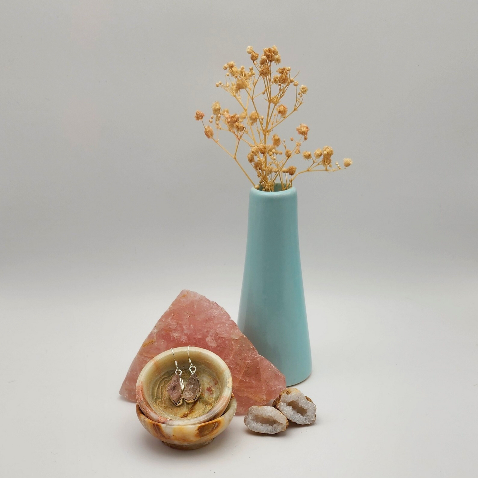 single pair of rough rose quartz earring sitting in an onyx bowl staged and arranged in a moody Bloom and Glow aesthetic scene.