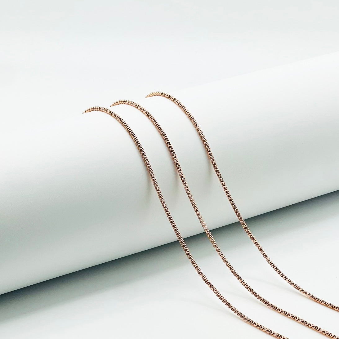 three rose gold popcorn chains draped over a white roll with a white background.