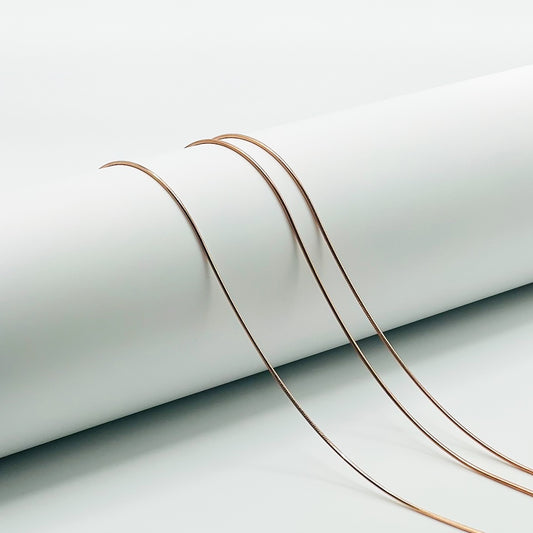 three rose gold snake chains are draped over a white cylinder with a white background
