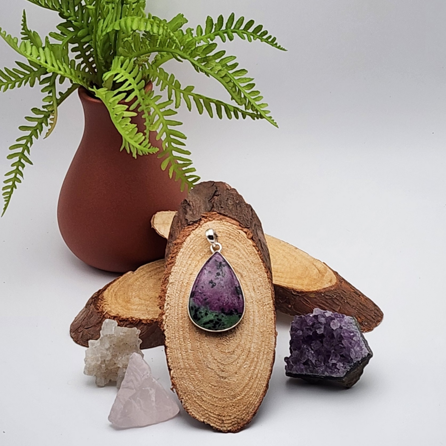 single zoisite pendant displayed on a sliced cross section of wood staged and arranged in a moody Bloom and Glow aesthetic scene.