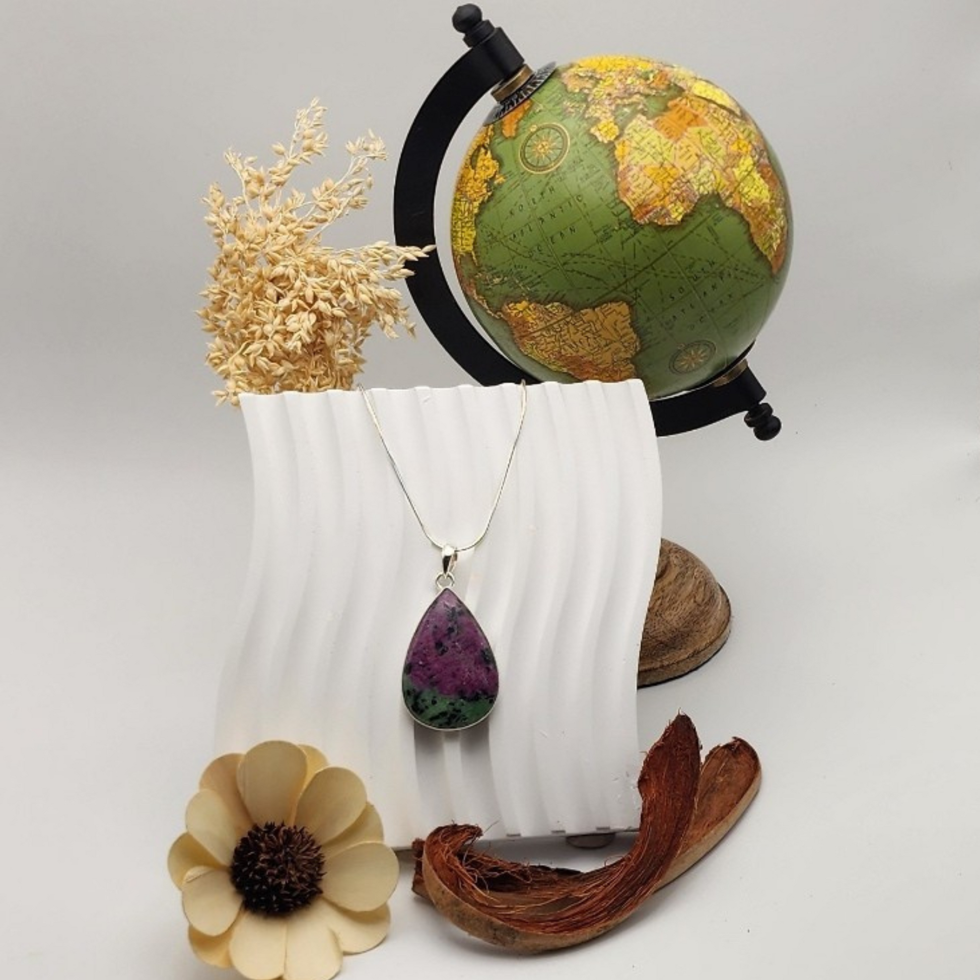 single ruby zoisite pendant displayed on a white squiggly ceramic piece staged and arranged in a moody Bloom and Glow aesthetic scene. 