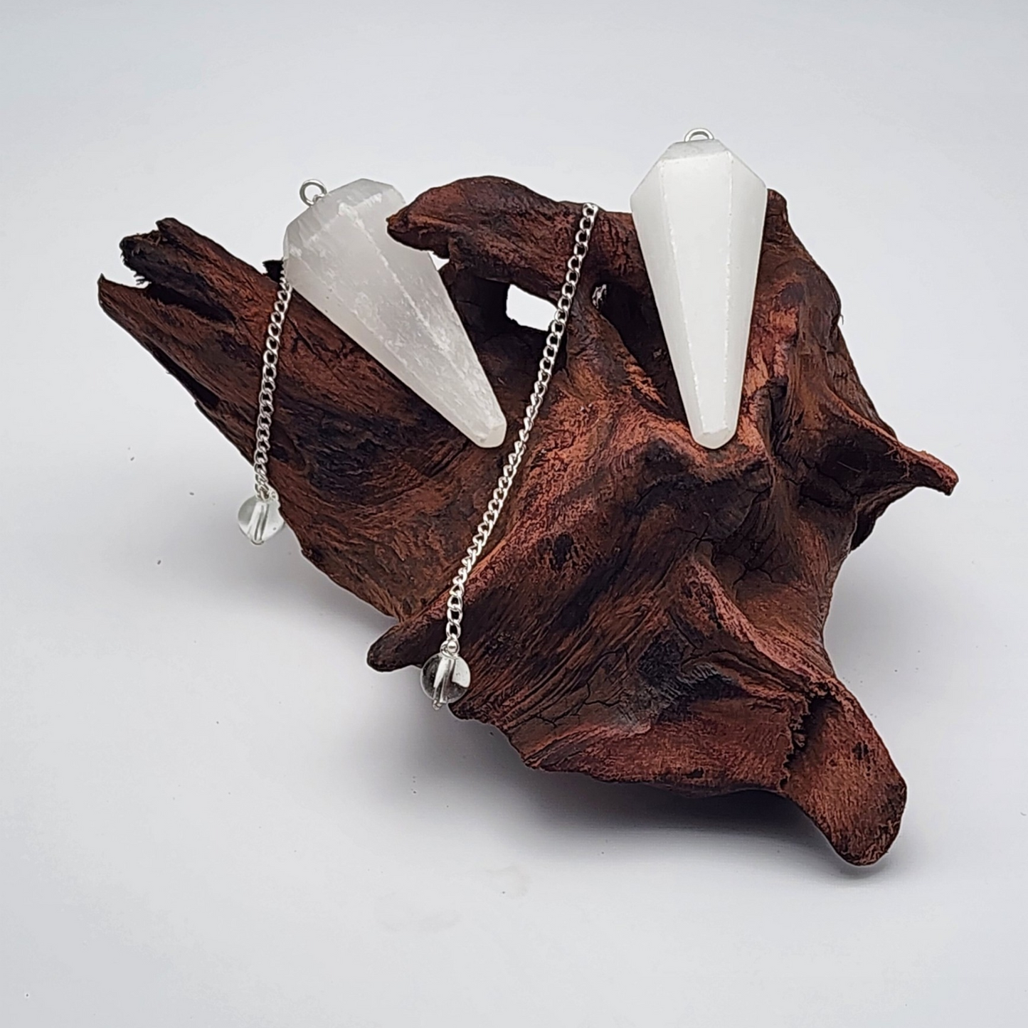 two selenite pendulums placed on an aged piece of wood with chains visible