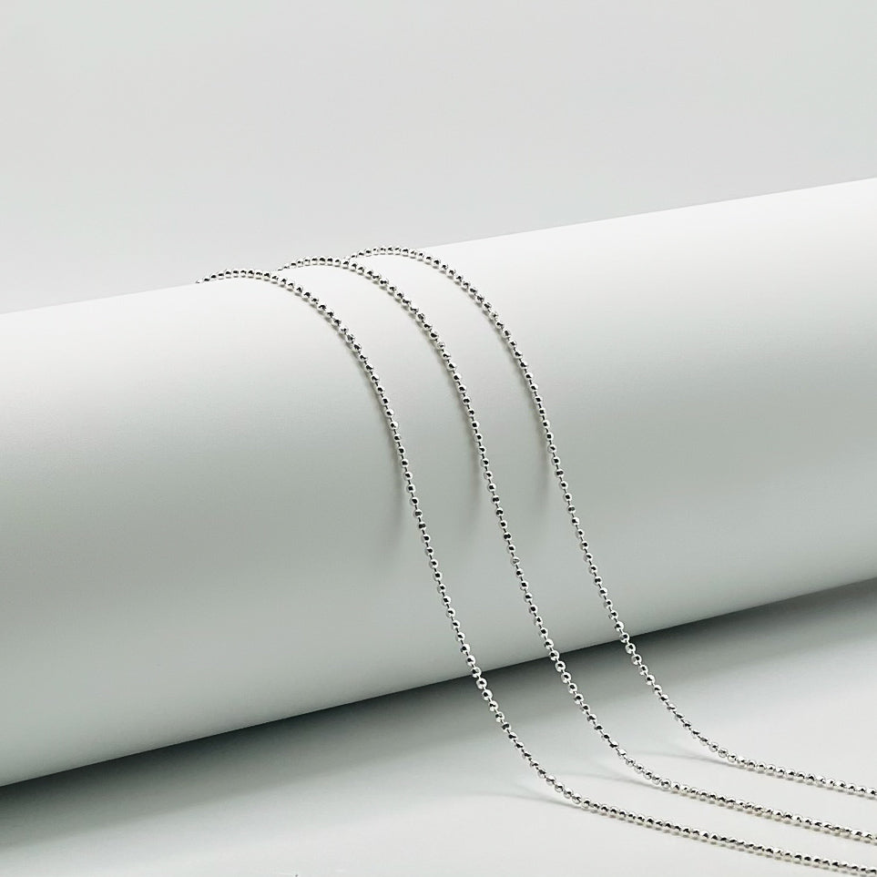 three ball chains draped over a while cylinder with a white background