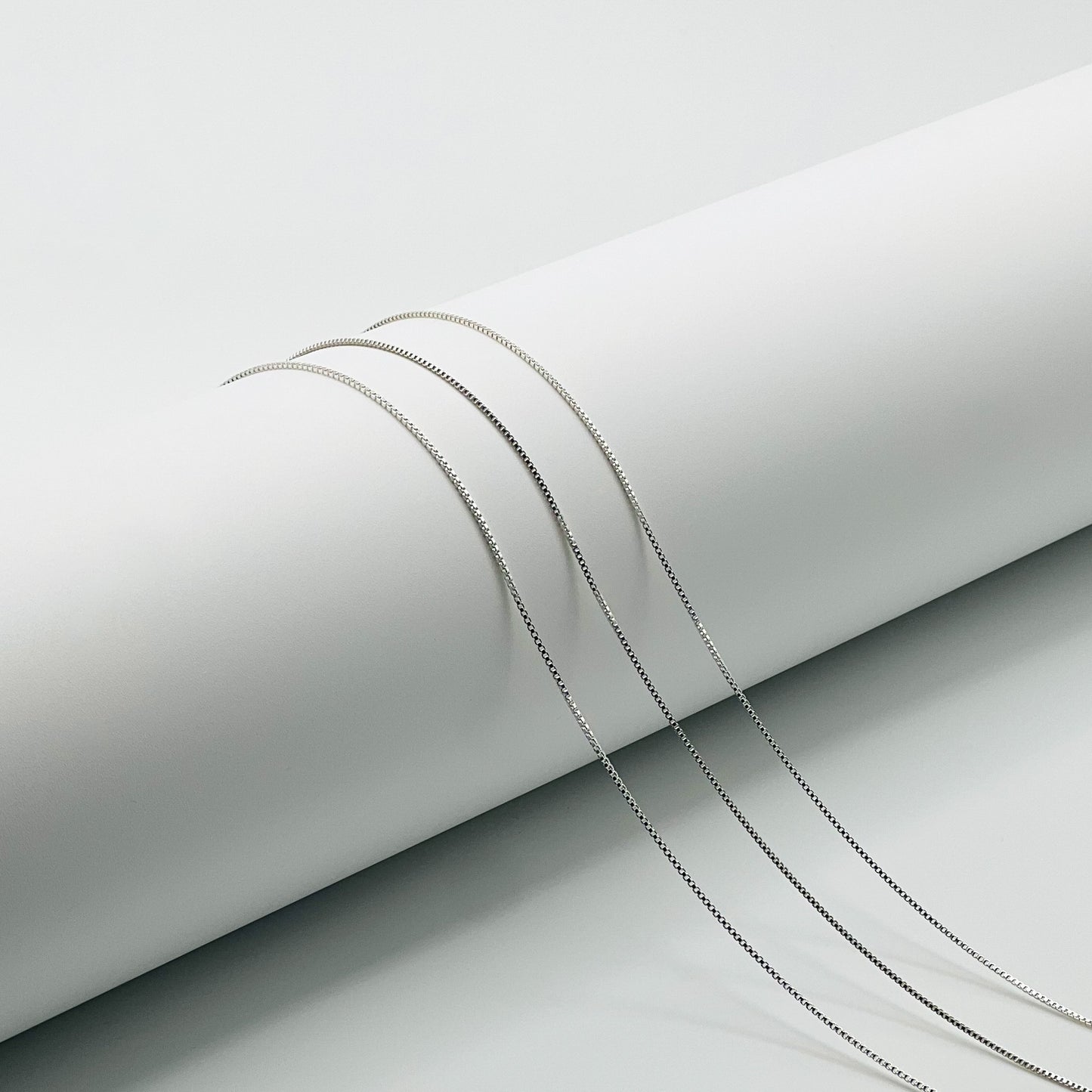 three silver box chains are draped over a white cylinder with a white background.