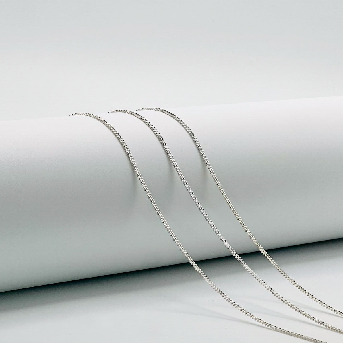 three curb chains draped over a white cylinder with a white background
