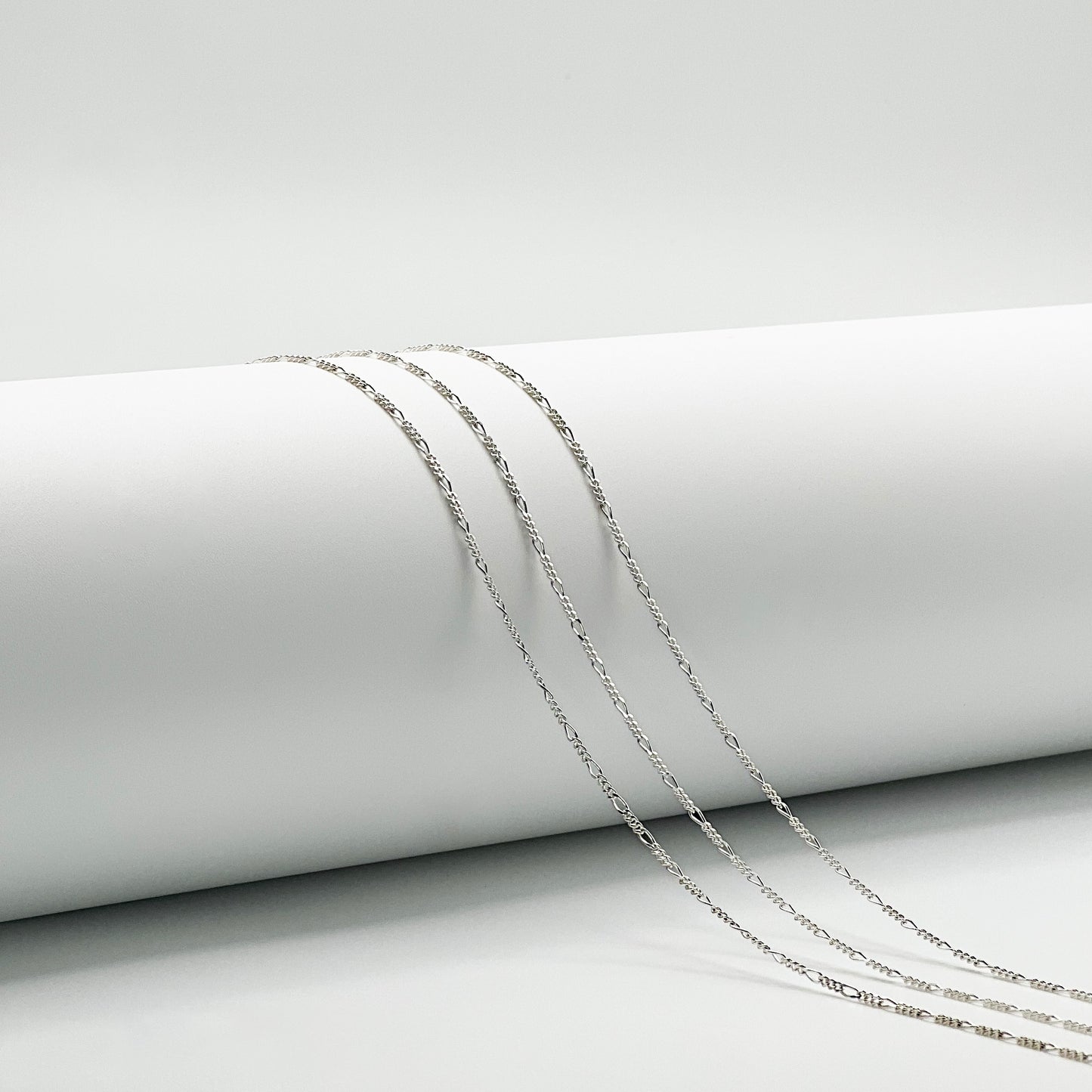 three figaro chain are draped over a white cylinder with a white background.