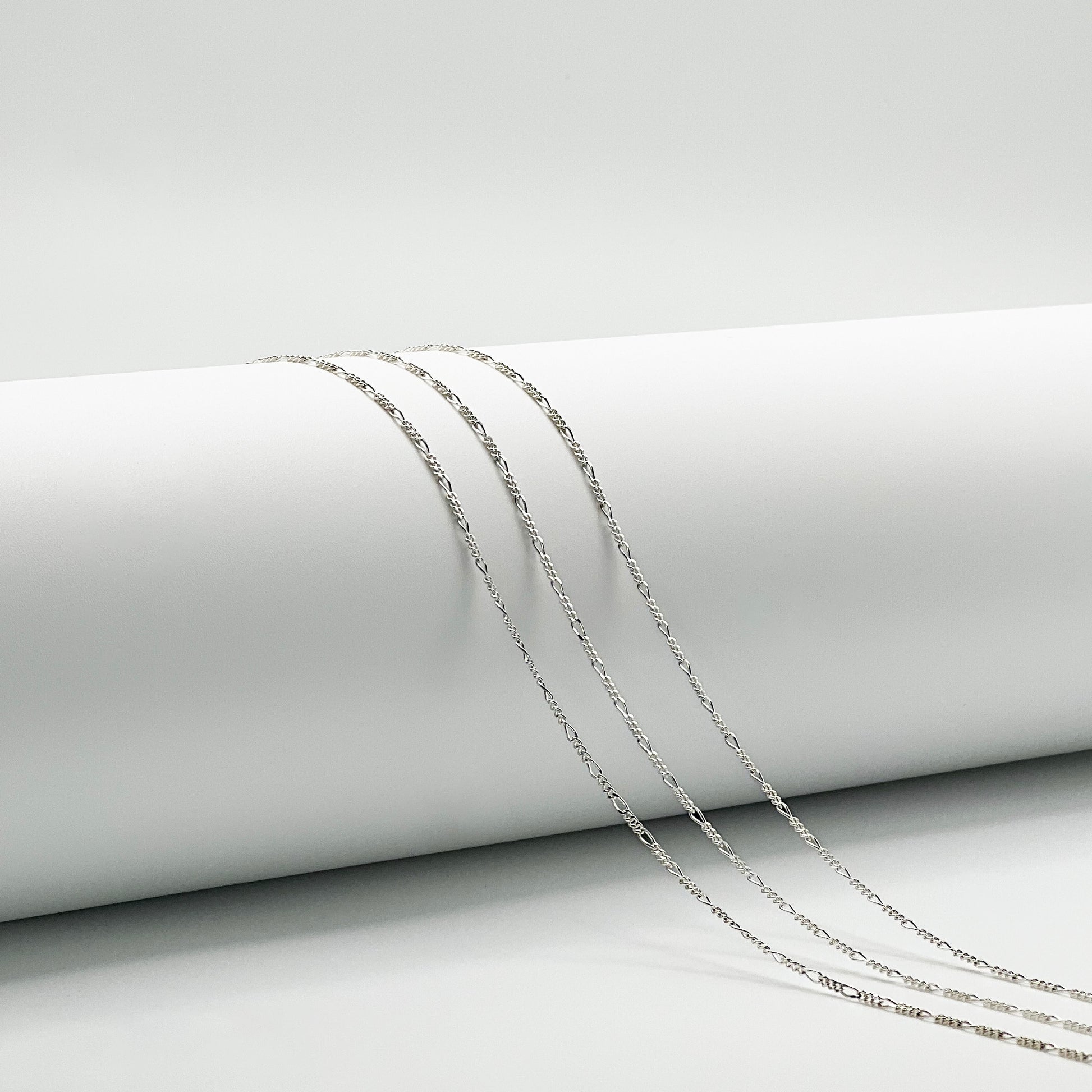 three figaro chain are draped over a white cylinder with a white background.