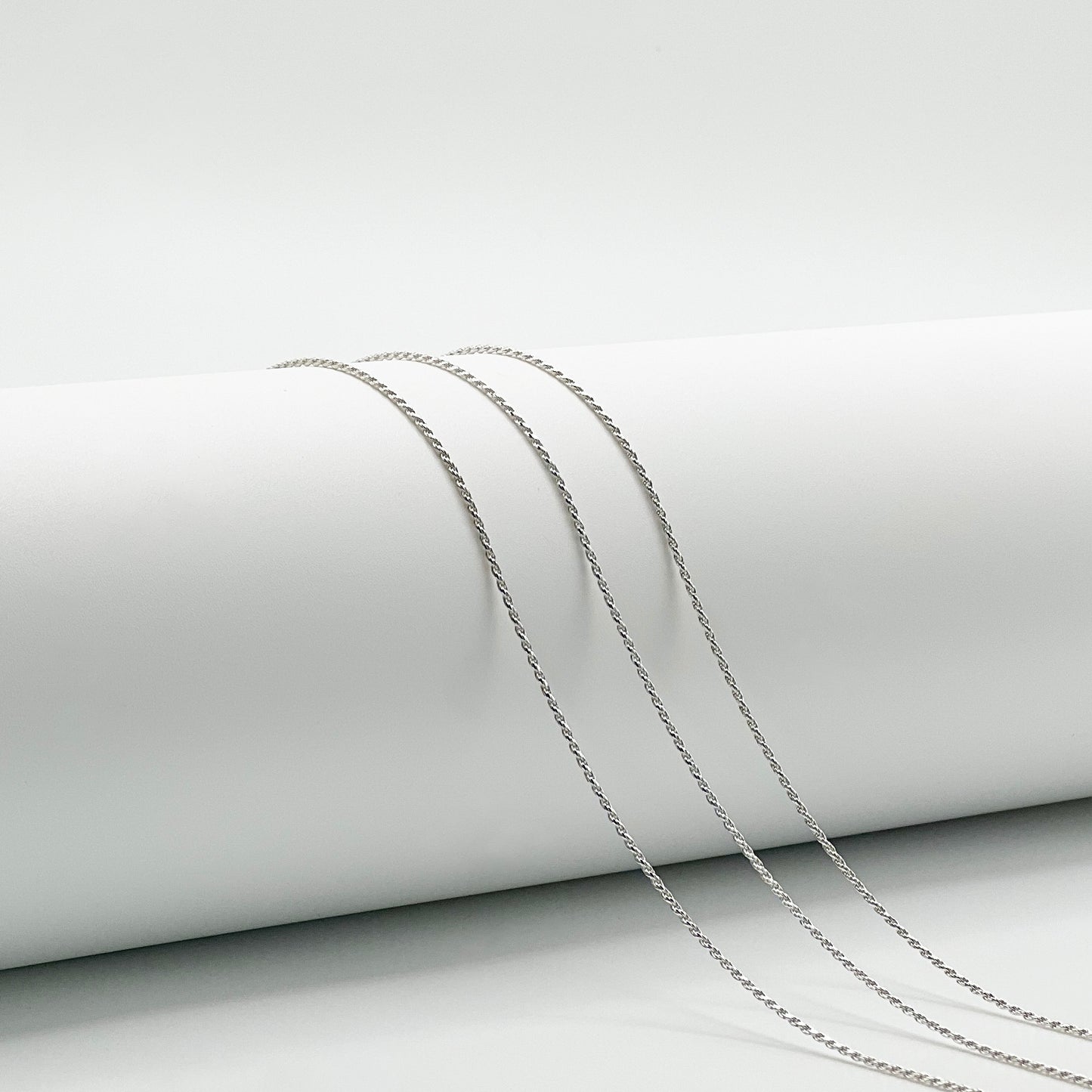three rope chains are draped over a white cylinder with a white background.