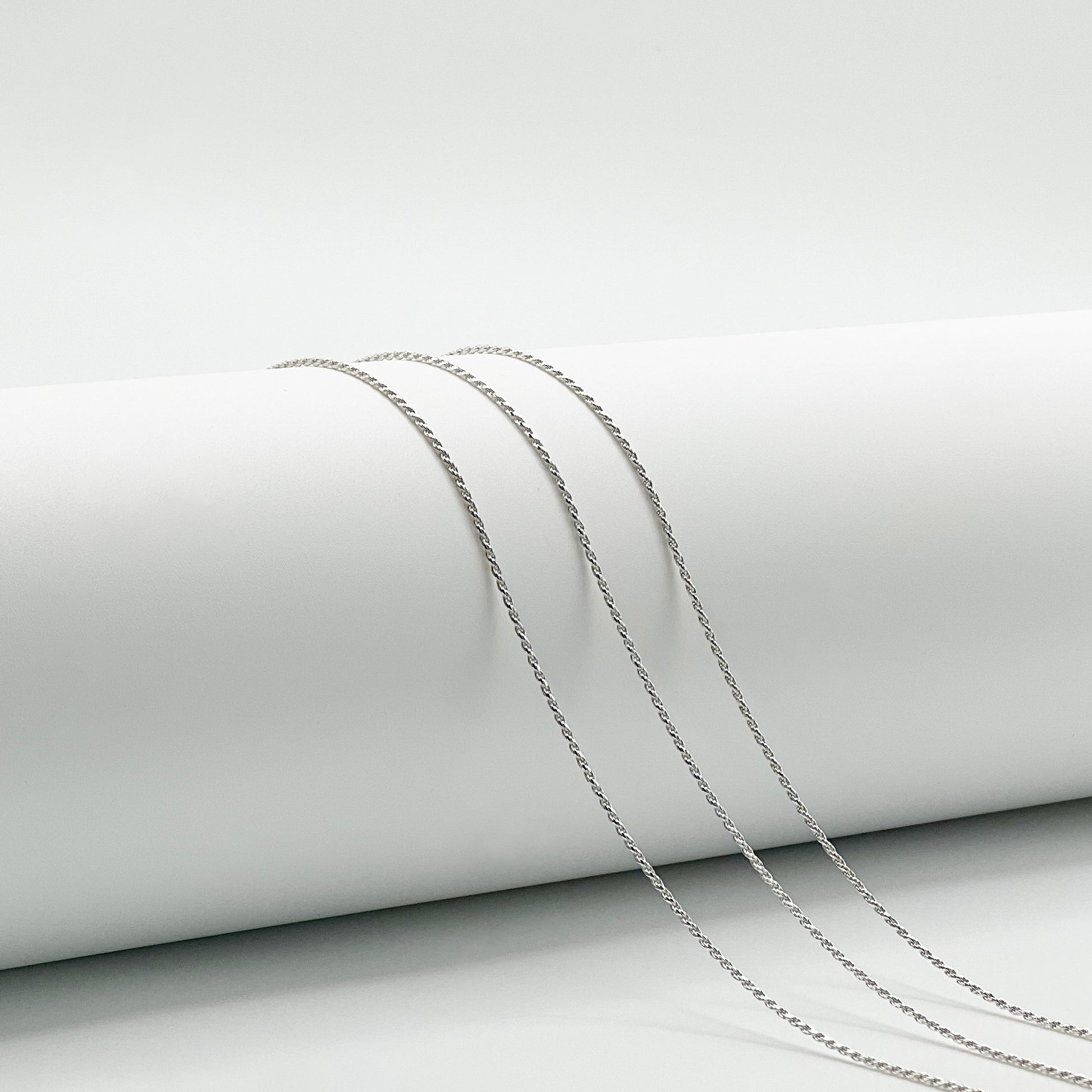three rope chains are draped over a white cylinder with a white background.