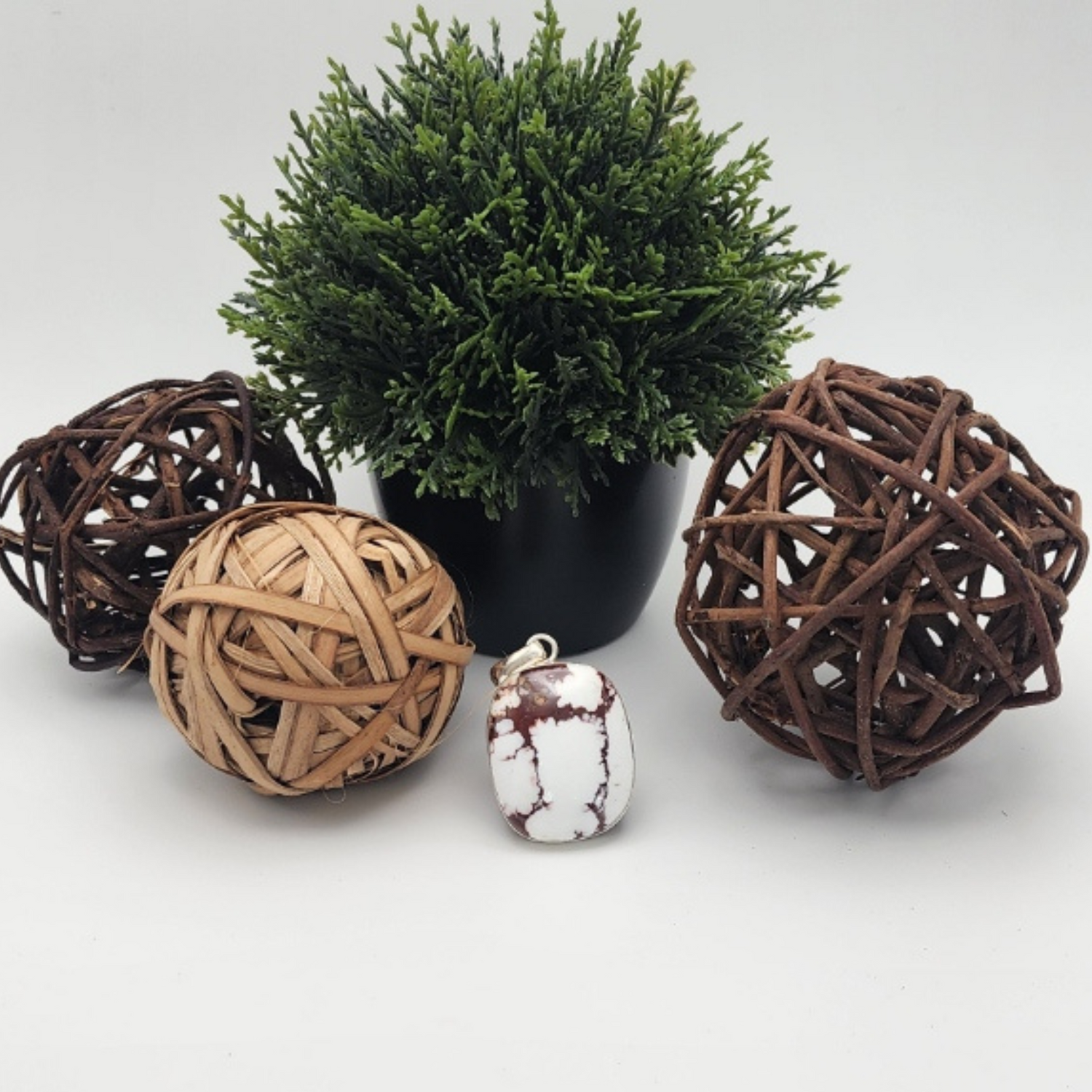 White Buffalo Turquoise pendant surrounded by decorative items including woven balls and a small potted plant on a white background.