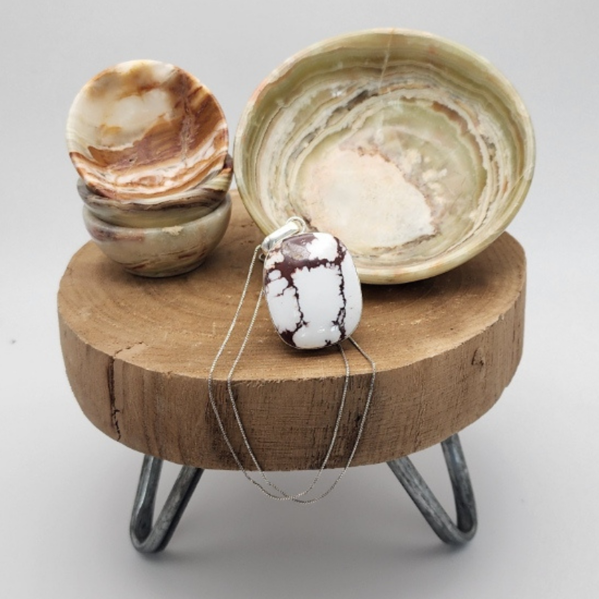 Small wooden table with two sizes of onyx bowls and a white buffalo pendant.