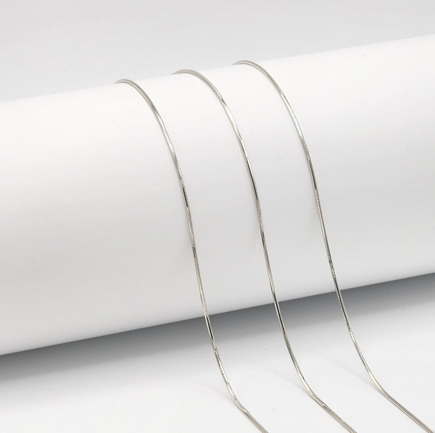 three silver snake chains draped over a  white cylinder with a white background.